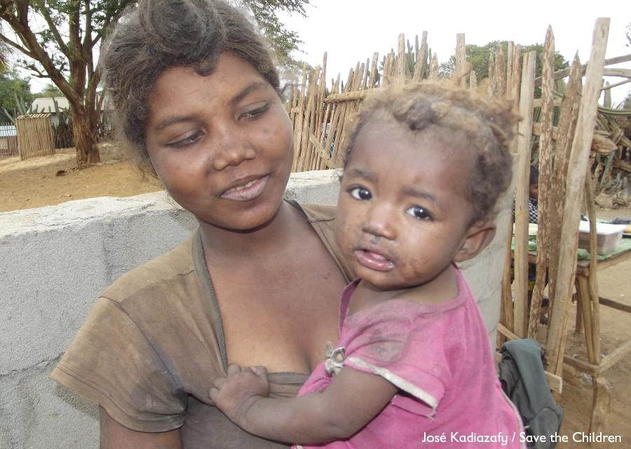 una mamma del Madagascar tiene in bracco sua figlia. La madre indossa una maglietta marrone, la bambina un vestito rosa. La piccola ha u braccio appoggiato al petto della madre e guarda in camera grata verso l obiettivo, la madre guarda la bambina.
