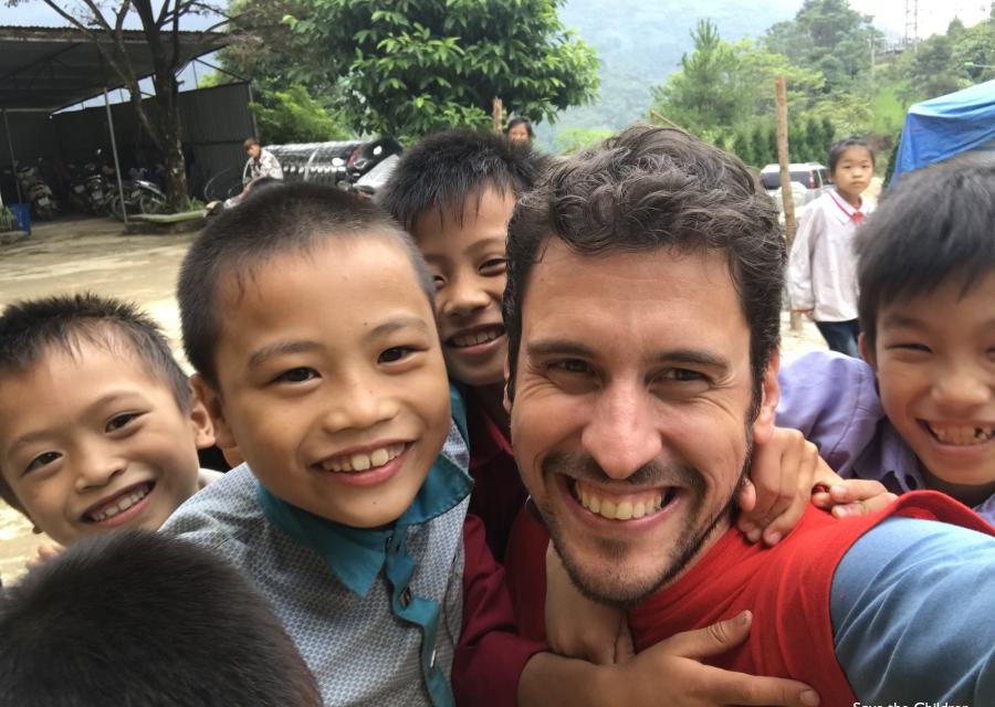 dipendente di Save the Children Italia sorridente circondato da bambini sorridenti
