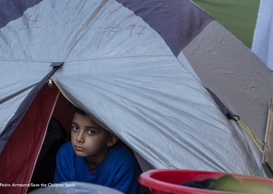 bambino si affaccia fuori a una tenda da campeggio in un campo profughi greco