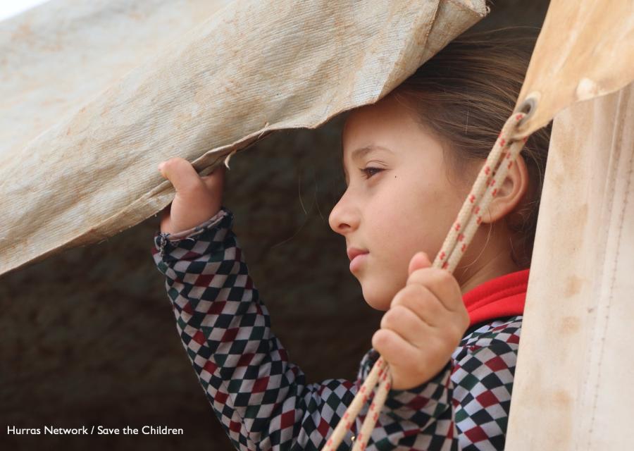 bambina siriana guarda verso sinistra attraverso una tenda che tiene aperta con una mano