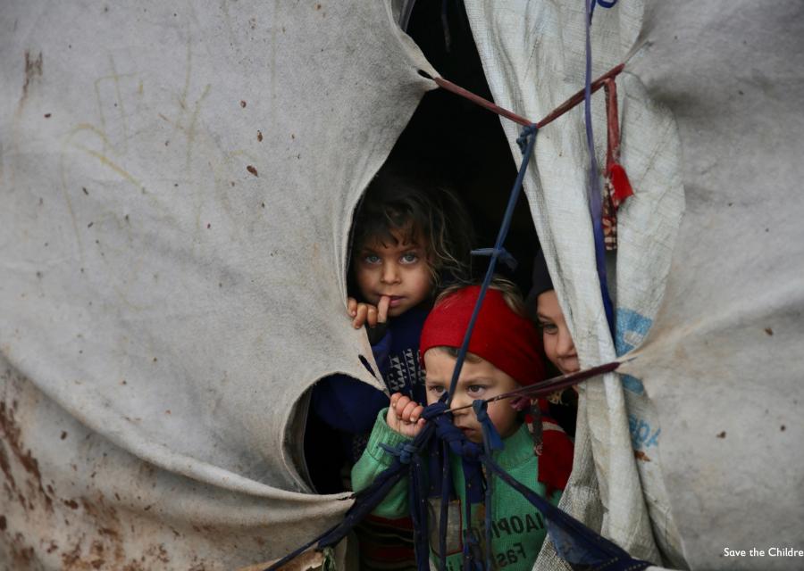 tre bambini siriani sfollati si affacciano dalla fessura di una tenda
