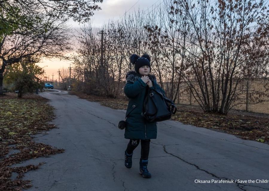 Una bambina ucraina vestita di blu con cappello di lana cammina su una strada in cemento alberata