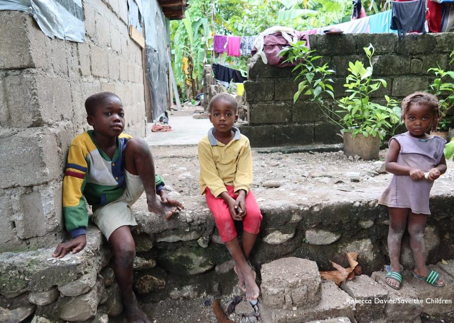 Tre bambini haitiani seduti su un gradino guardano in camera