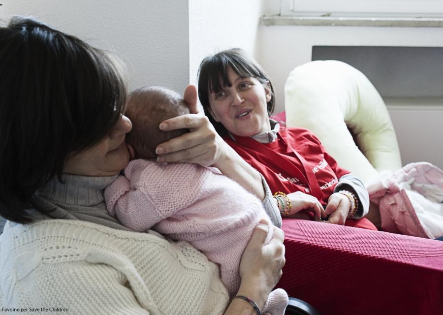 Madre che tiene in braccio un neonato accanto ad una operatrice di Save the Children