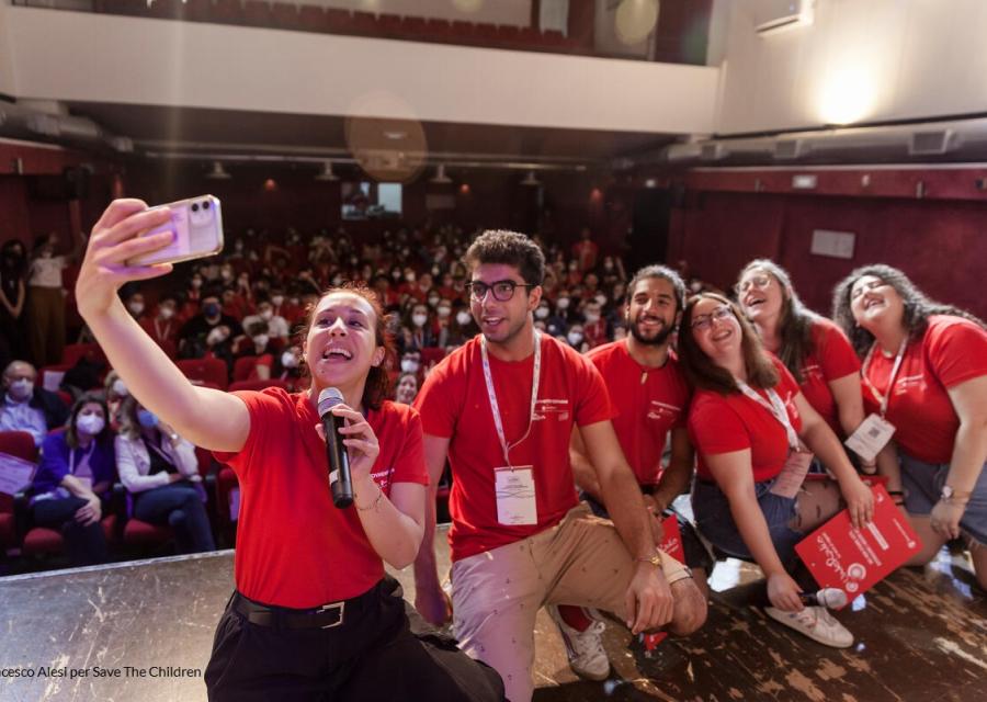 ragazzi volontari di save the children su un palco mentre scattano un selfie insieme ad altri volontari 
