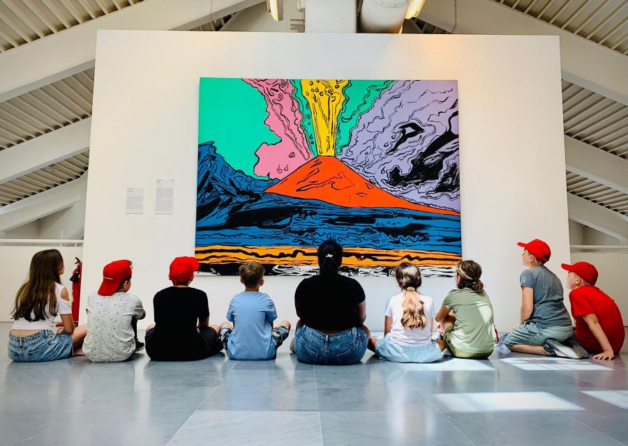 studenti e studentesse seduti a terra mentre guardano un quadro di un vulcano