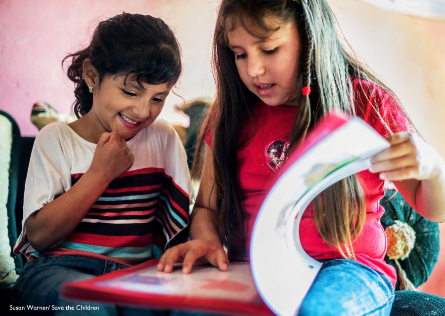due bambine leggono insieme un libro. Una con i capelli castano scuro raccolti e l'altra con i capelli castano chiaro sciolti.