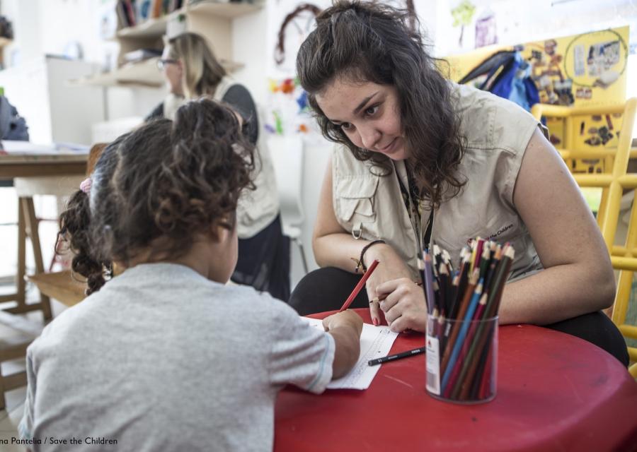 operatrice seduta a un piccolo banco della scuola dellinfanzia con una bimba mentre colorano insieme