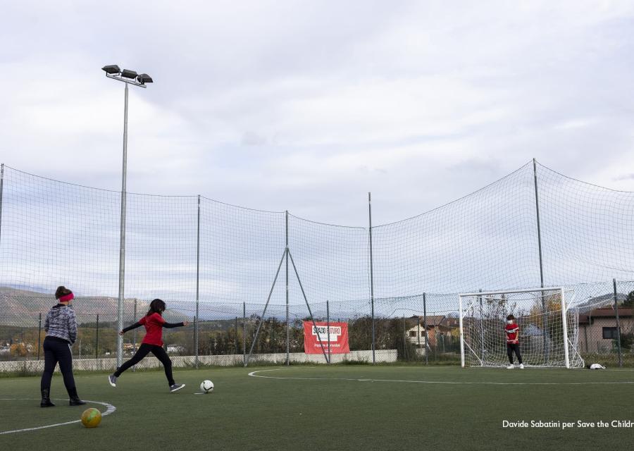 campetto di calcio con due bambini che giocano in lontananza, uno con maglietta rossa e pantaloni neri l altro con maglietta grigia e pantalone nero
