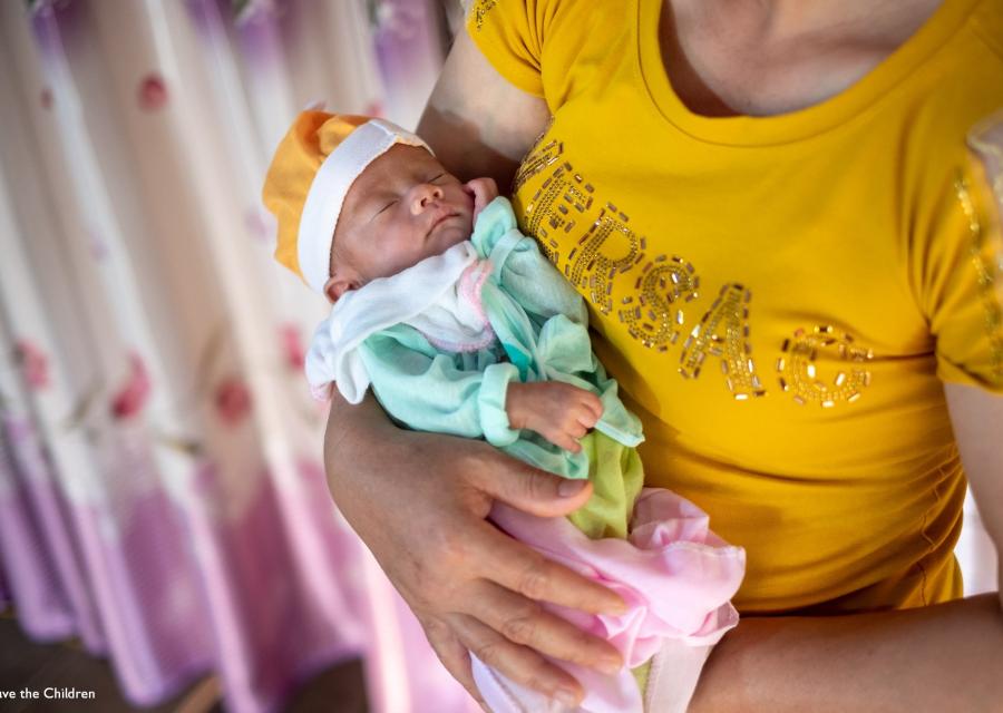 neonato con berrettino e tutina in braccio ad una donna