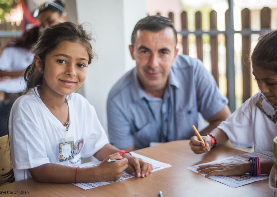 uomo adulto tra due bambine seduti a un tavolo a colorare e disegnare insieme, tutti sorridenti