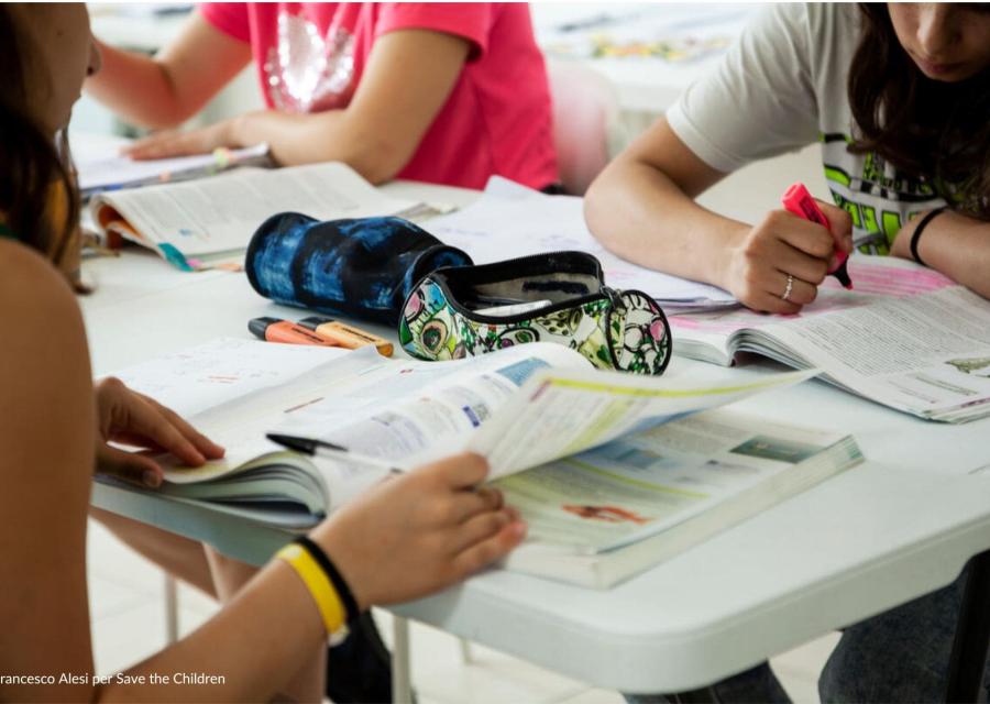 Adolescenti durante attività di accompagnamento allo studio nel Punto Luce di Potenza di Save the Children che scrivono sui libri 