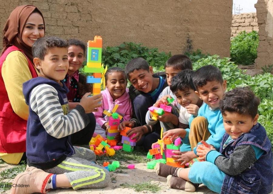 bambini afghani seduti a terra in cerchio mentre giocano sorridenti alle costruzioni insieme a operatrice save the children 