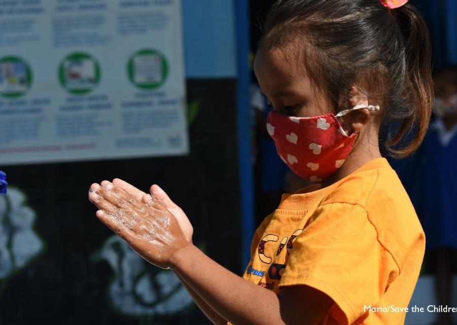 bambina indonesiana di profilo si lava le mani mentre indossa mascherina colorata sul viso.