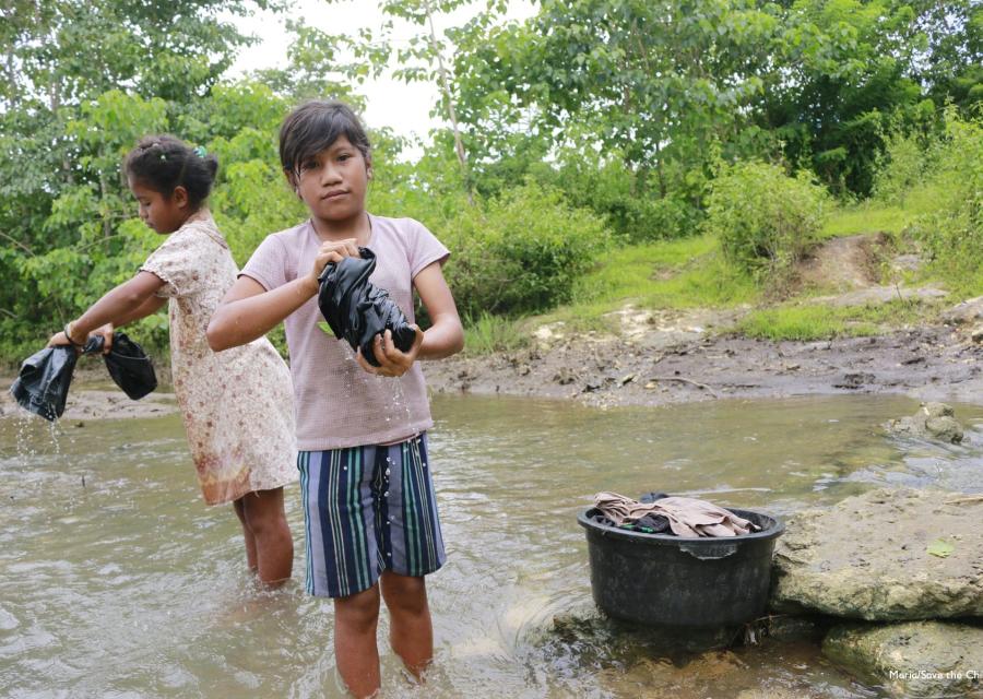 Due bambine indonesiane in piedi in un torrente strizzano i panni