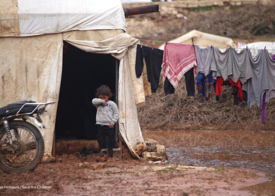 bambina che si copre il viso di fronte alla sua tenta dopo le inondazioni in Siria