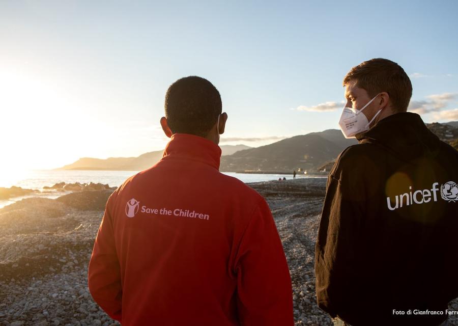 Due operatori, uno save the children e  l altro Unicef, di spalle guardano un tramonto davanti a loro.