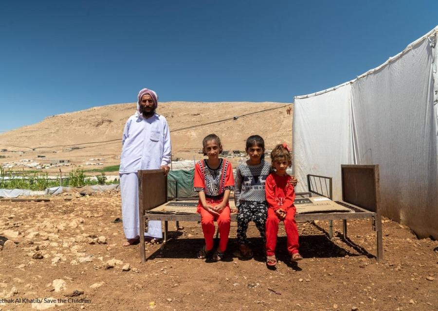 tre bambini yazidi seduti su una panca e in piedi alla loro destra il padre vestito di bianco 