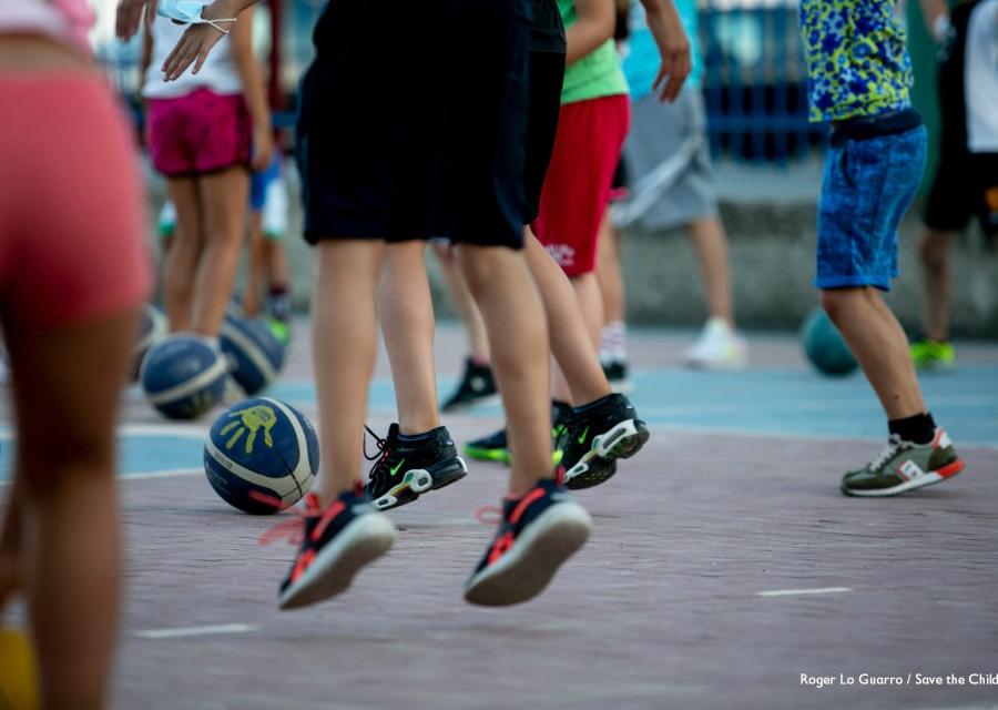 Primo piano di gambe di bambini e bambine che giocano con la palla in un campo da basket