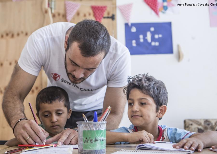 operatore umanitario in piedi aiuta due bambini seduti al banco di scuola a fare i compiti