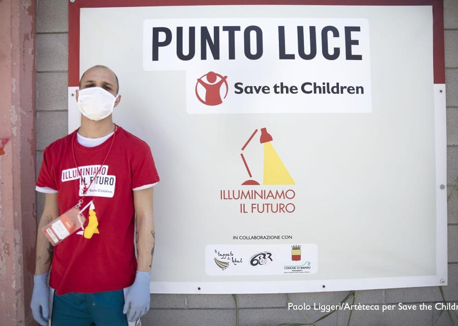 Un operatore save th children posa davanti al cartello di ingresso del Punto Luce di Napoli Barra.