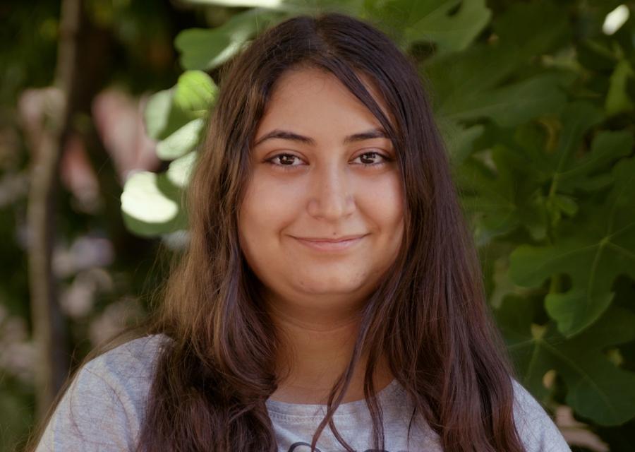 Primo piano di una ragazza bruna con capelli lunghi. Lei indossa una maglietta grigia ed è sorridente