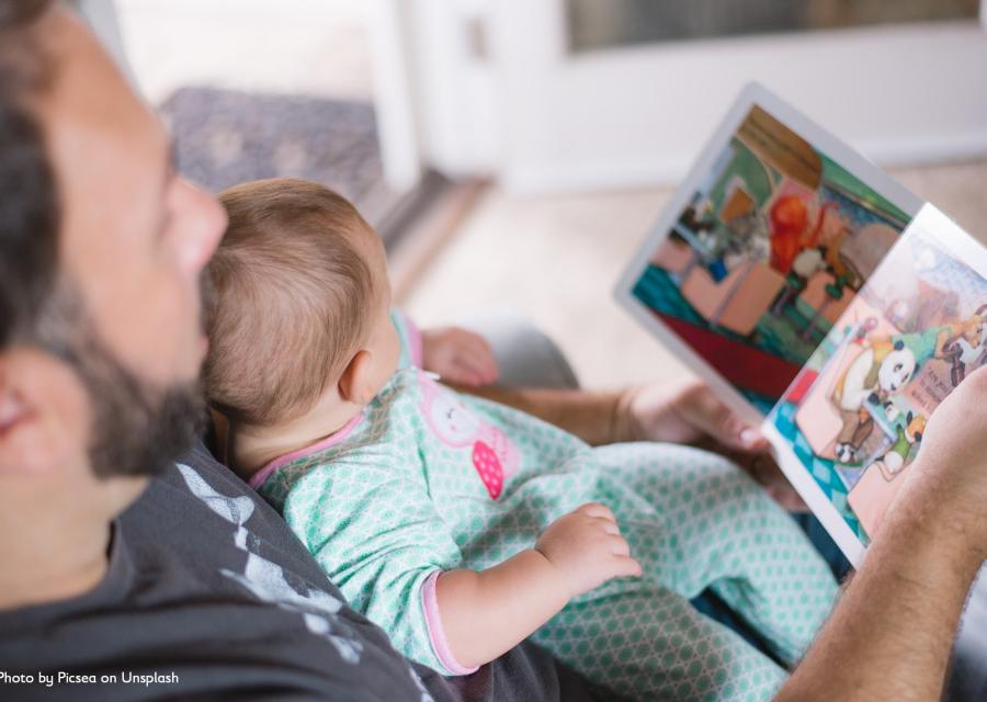 bimba neonata in braccio al papà mentre leggono insieme un libro illustrato