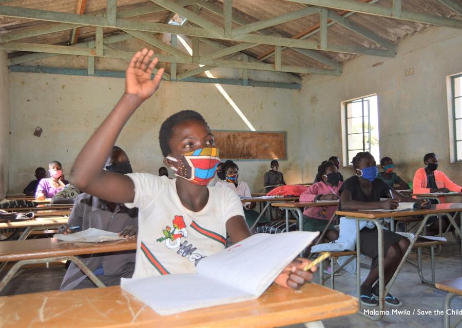 Bambina dello Zambia con la mascherina seduta al banco in classe con mano alzata