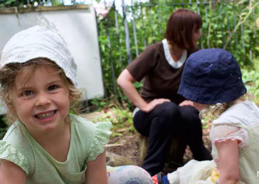 bimba sorridente in primo piano, sullo sfondo altri bambini e bambine che giocano insieme