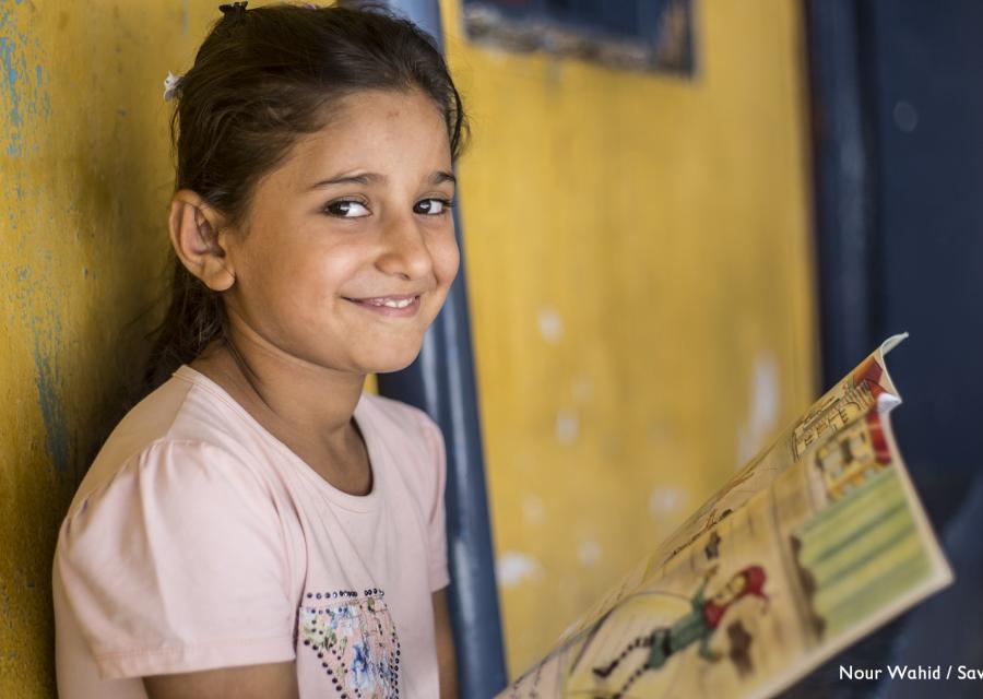 Bambina sorridente guarda in camera mentre tiene in mano un libro aperto e colorato