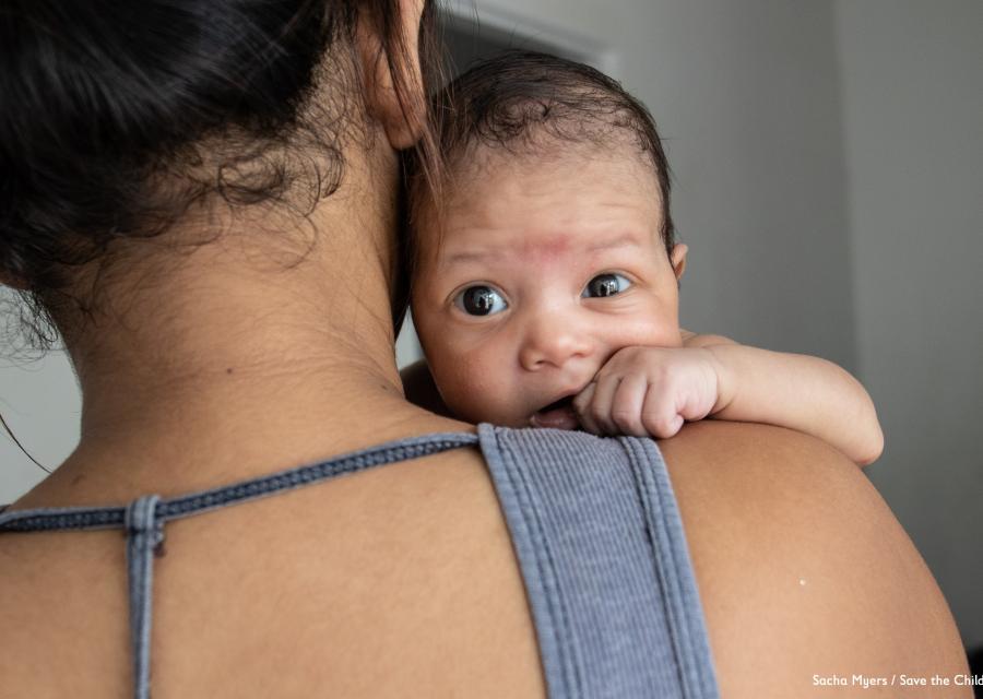 mamma di spalle con in braccio il suo neonato che guarda in camera
