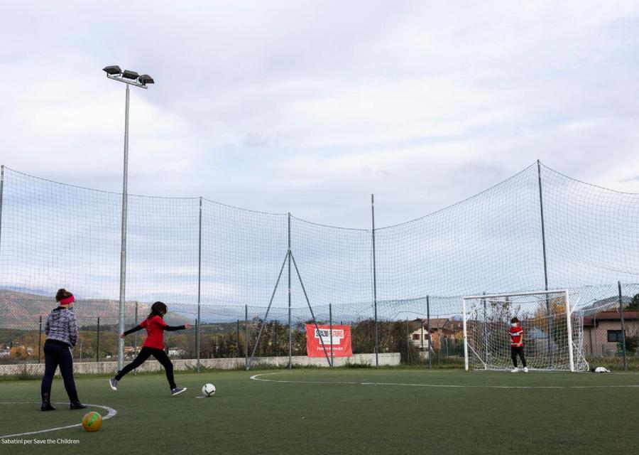 campo da calcio in cui giocano 3 bambini e una di loro si appresta a tirare in porta