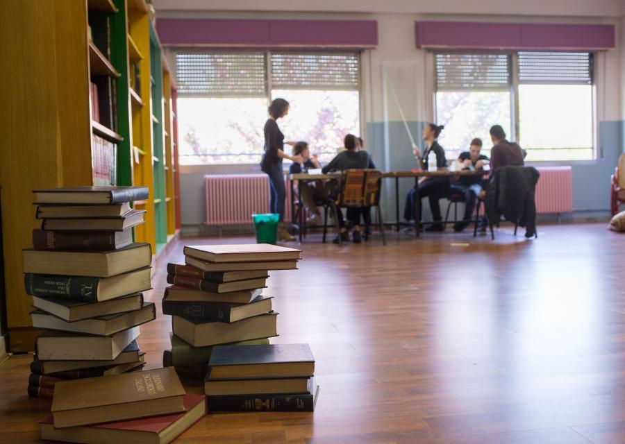biblioteca, in primo piano dei libri accatastati e sullo sfondo delle persone intorno a un tavolo