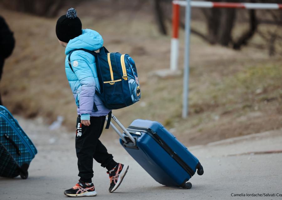 bambino vestito con vestiti invernali con trolley e zaino sulle spalle cammina per strada