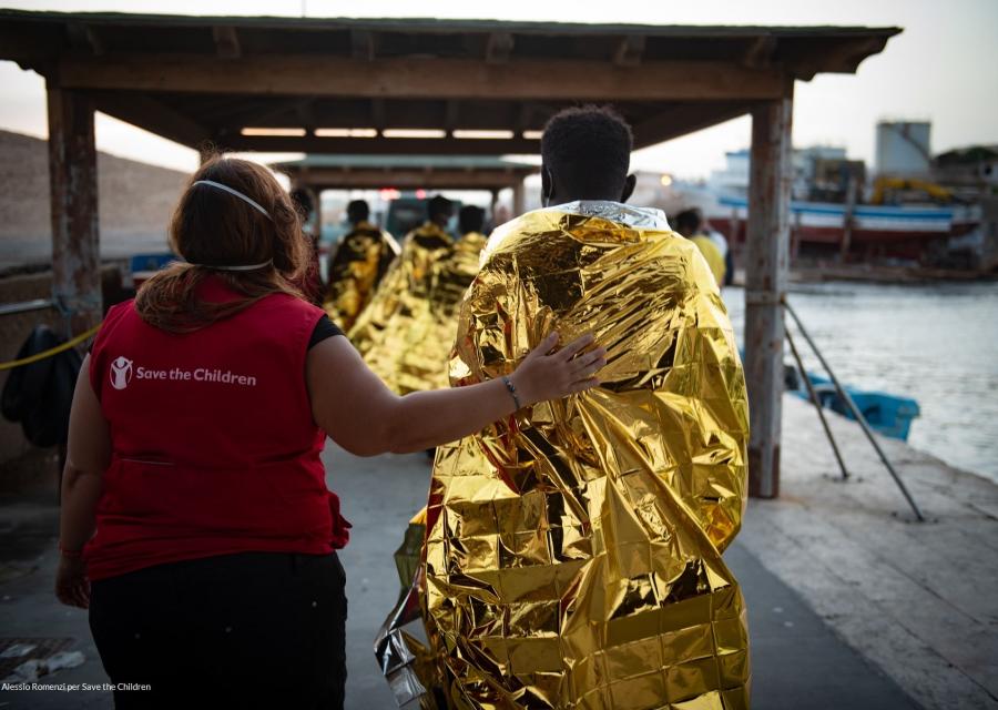 Foto di un ragazzo migrante avvolto in una coperta termica accanto ad una nostra operatrice