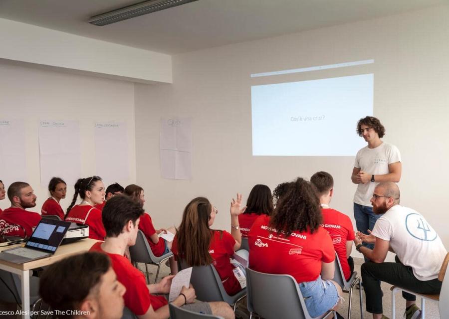 giovani seduti ad ascoltare la lezione di un loro coetaneo 