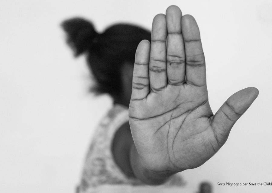 In primo piano la mano aperta in segno di stop di una ragazza nigeriana. Dietro la mano si intuisce un profilo di donna