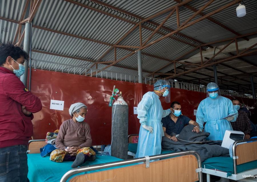 Stanza di ospedale in Nepal in cui si trovano due pazienti seduti sul letto e la mascherina e alcuni operatori vicino a loro.