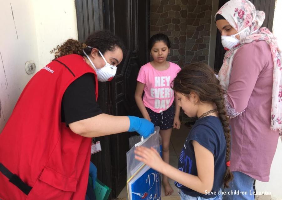 Operatrice save the children di spalle distribuisce kit scolastici a bambini libanesi