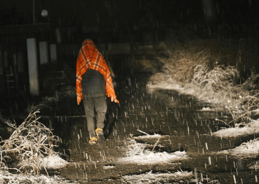 ragazzo di spalle che cammina con coperta sulle spalle sotto la neve