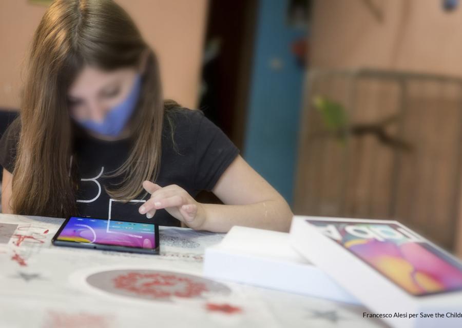ragazza adolescente si vede sfocata ed è china su un tablet appoggiata su un tavolo.