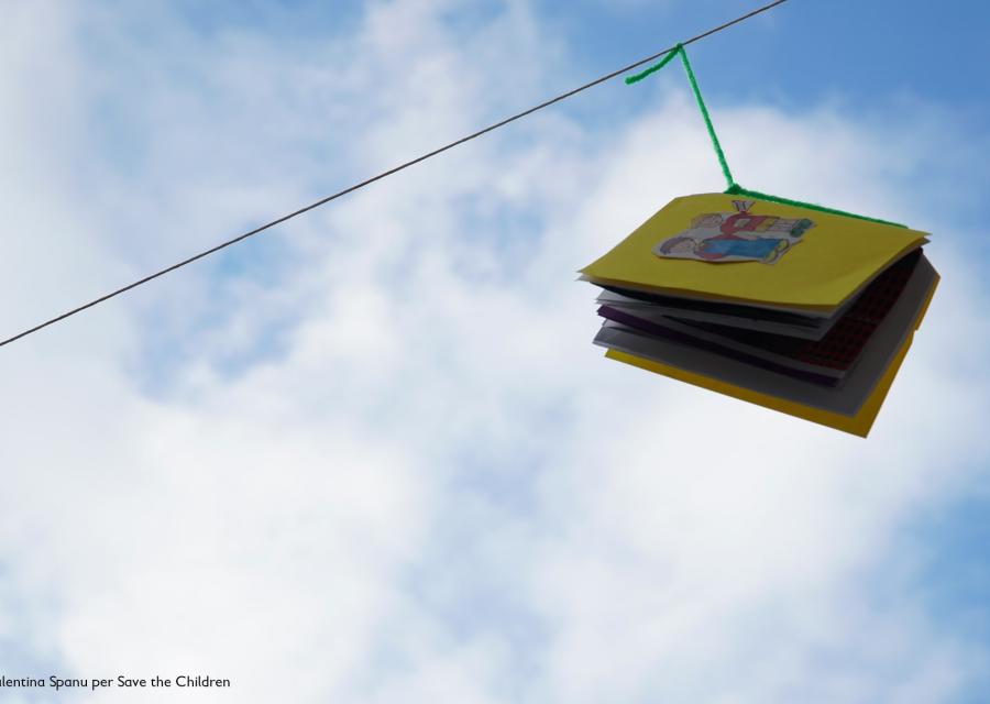 libro colorato appeso a un filo in esterno, sullo sfondo un cielo azzurro con nuvole bianche