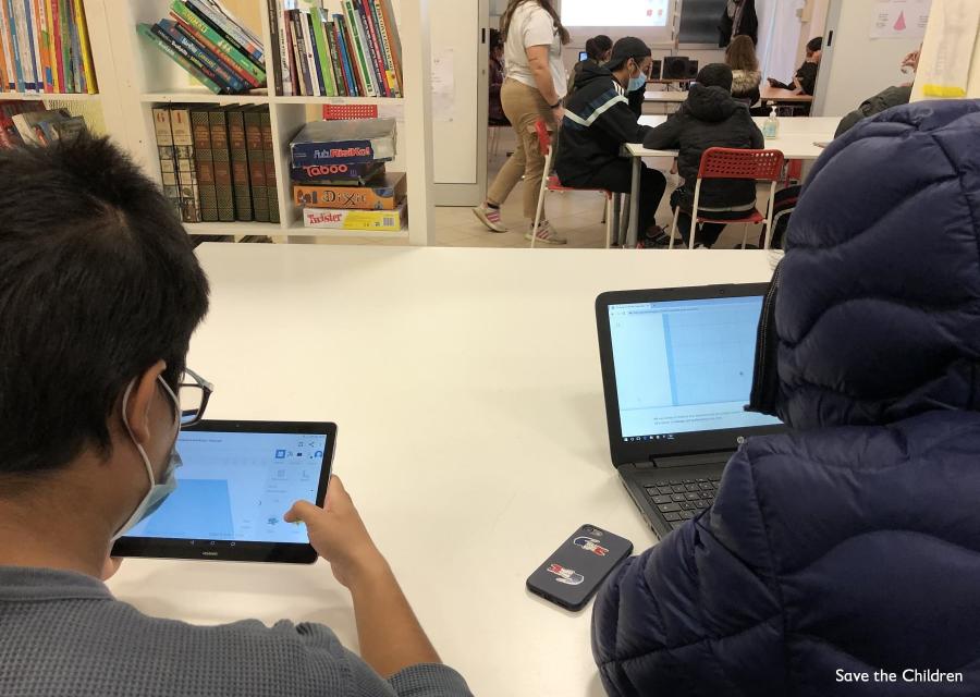 Due bambini di spalle seduti a una scrivania digitano uno su un tablet e uno su un pc.
