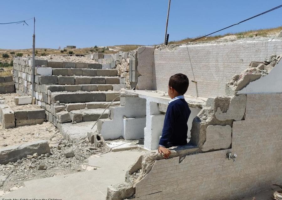 bambino palestinese di spalle con maglietta blu che guarda le macerie di una casa distrutta