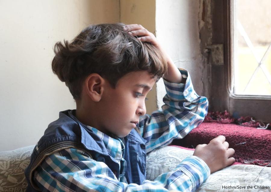 Bambino yemenita seduto di profilo vicino a una finestra guarda verso il basso