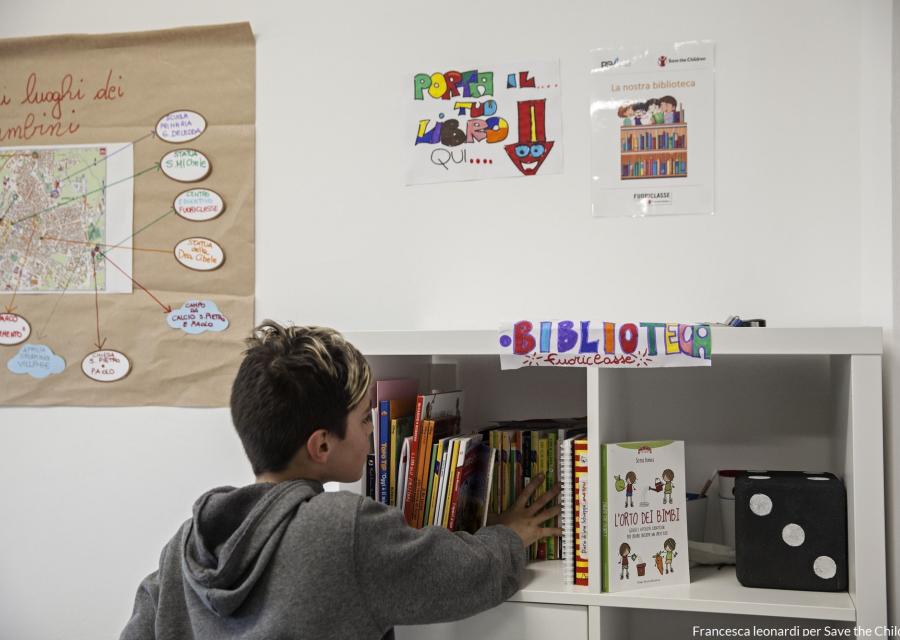 bambino con felpa grigia prende un libro da uno scaffale dedicato ai libri in unaula scolastica