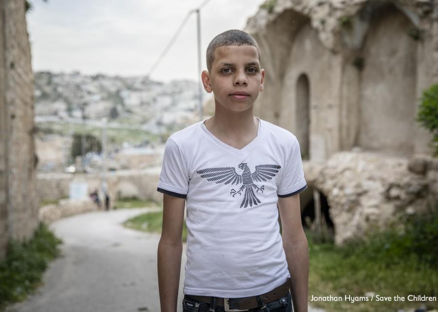 bambino dei territori palestinesi occupati ripreso a mezzo busto con maglietta bianca e sfondo paesaggio sfocato