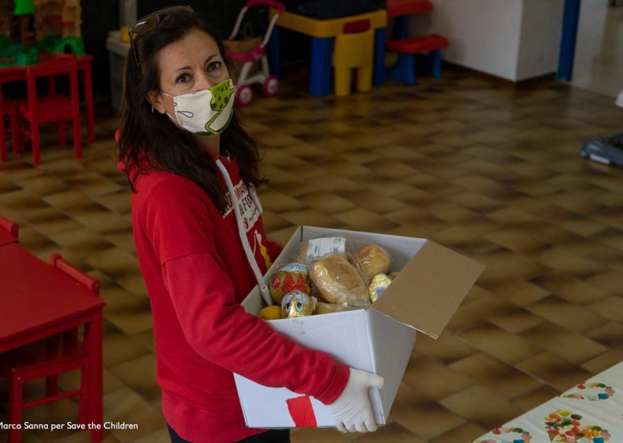 Operatrice save the children con pacco spesa in mano per famiglie vulnerabili durante emergenza coronavirus