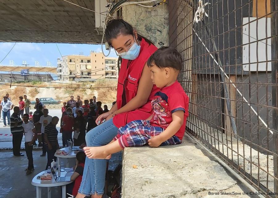 Operatrice Save the Children seduta su un muretto insieme a un bambino accanto a lei
