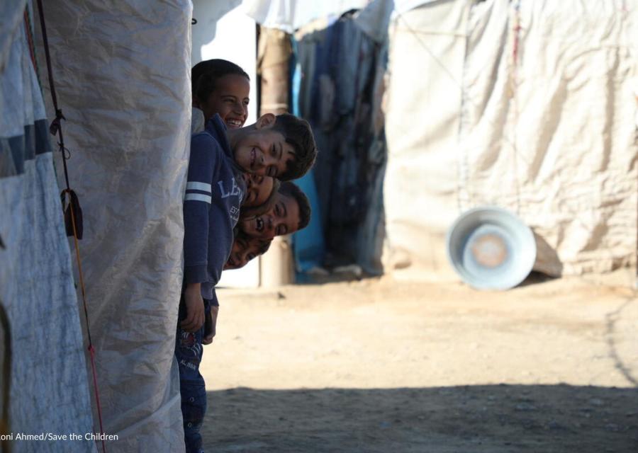 quattro bambini siriani sorridenti che spuntano fuori da una tenda Save the Children 